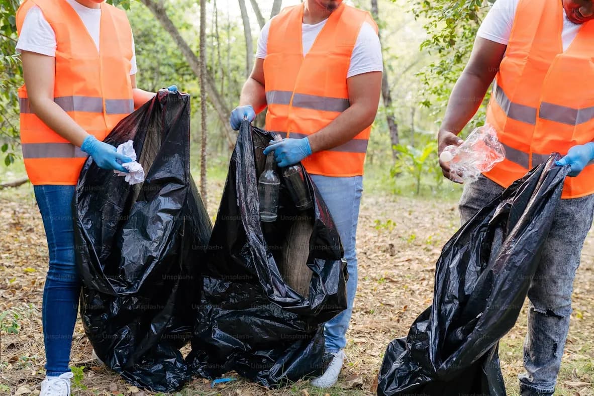 Three collectors in high-visibility vests holding bags of sorted waste after a neighbourhood pickup
